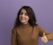 smiling young beautiful girl wearing brown turtleneck sweater showing thumb up isolated on purple background